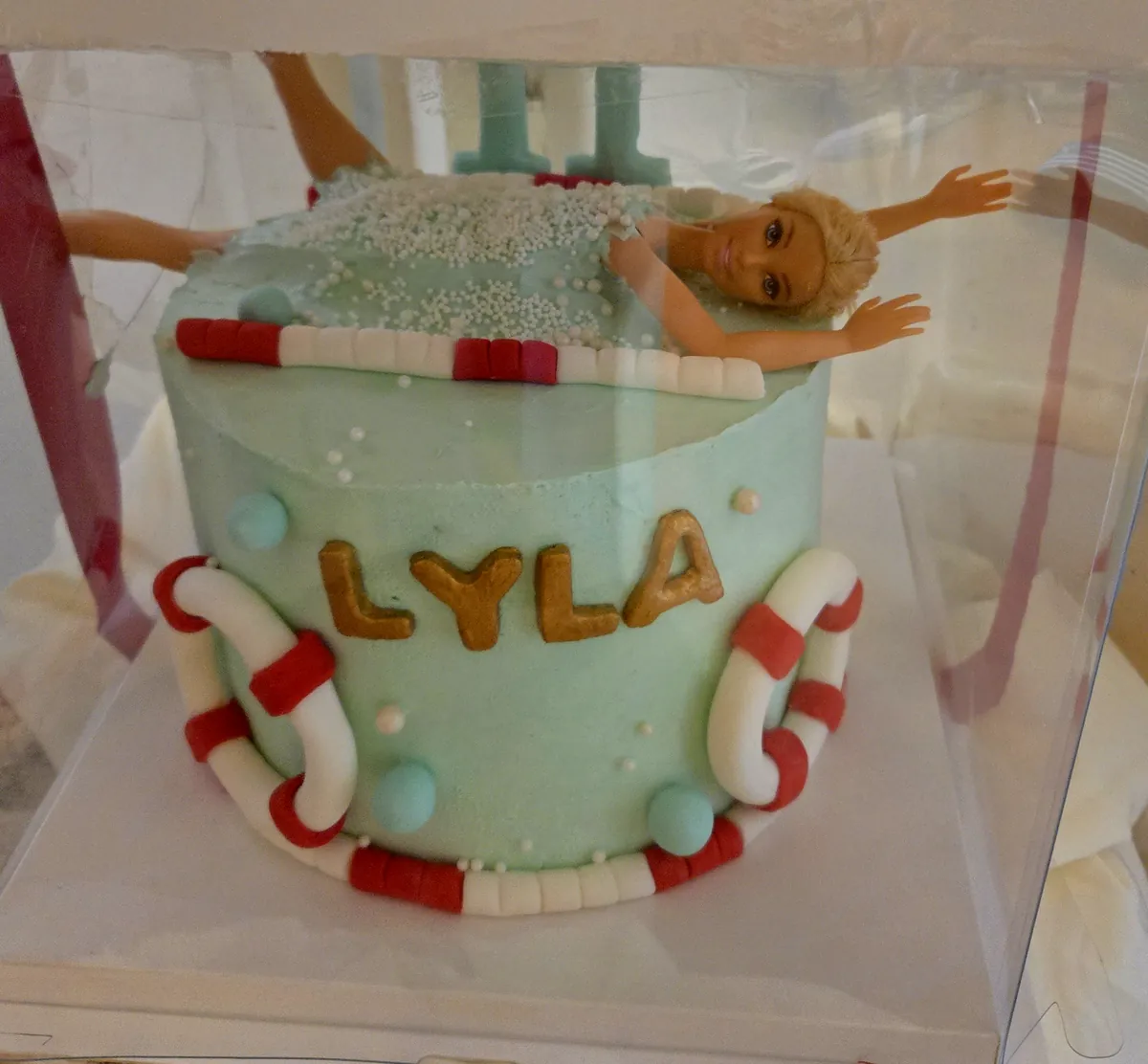 Gâteau Barbie piscine pour les 11 ans de Lyla : crème turquoise, Barbie qui plonge dans une écume de perles blanches, bouées rouges et blanches, lignes de nage et prénom Lyla en lettres dorées