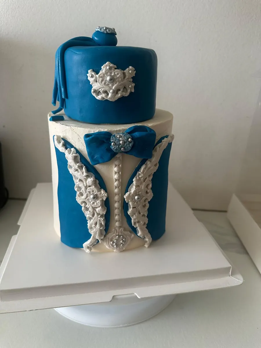 Gâteau de circoncision deux étages bleu et blanc : chapeau à pompon bleu, gilet bleu à broderies blanches, nœud papillon et perles argentées