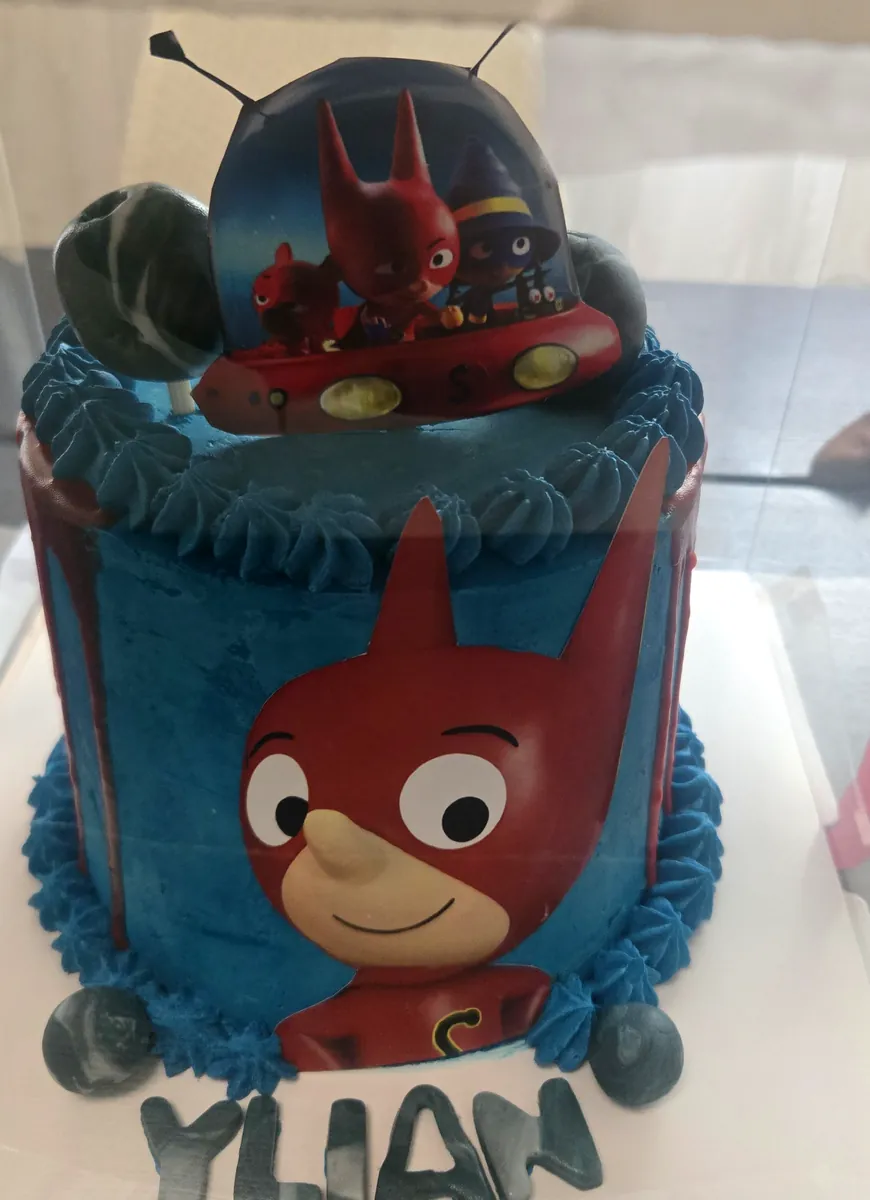 Gâteau à personnage imprimé : crème bleue, coulures rouges, Simon Super Lapin imprimé sur le côté, soucoupe volante en topper et prénom Ylian, la même technique que pour un gâteau Stitch